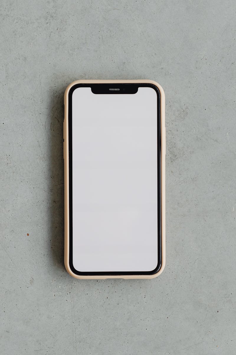 Top view of a modern smartphone with a blank white screen on a gray concrete background, ideal for mockups.